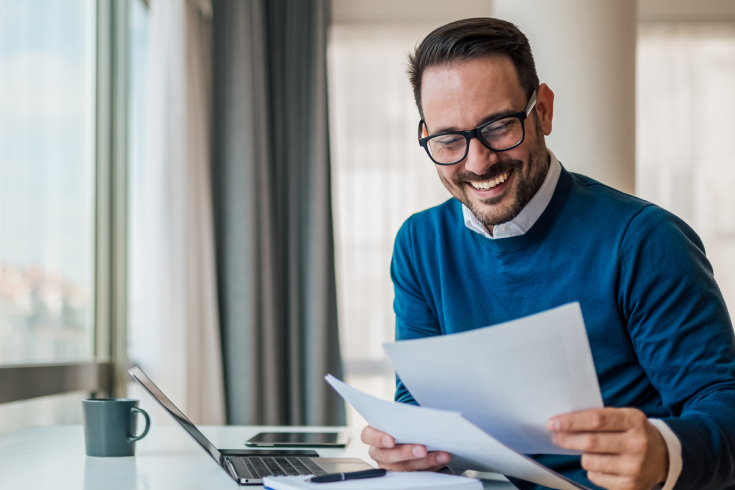 Man in glasses smiling, holding paper.