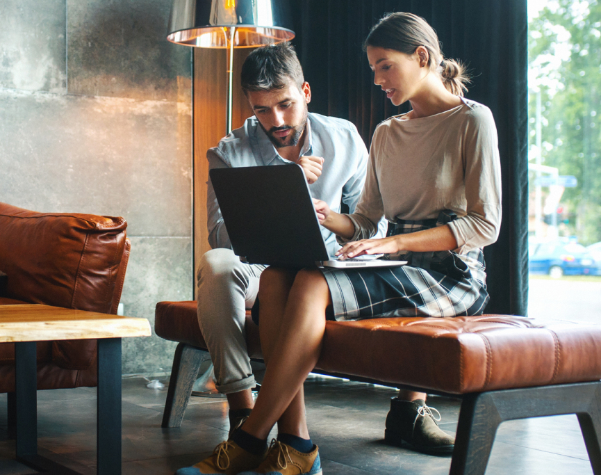 A man and woman sitting on a bench with a laptop.