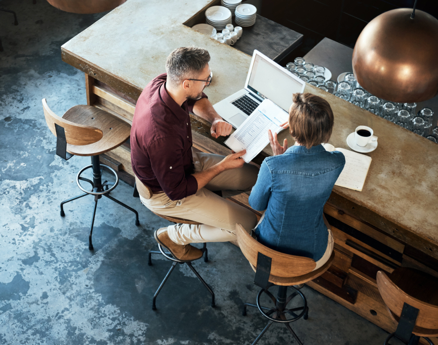 Two individuals sitting at a bar, working on a laptop.