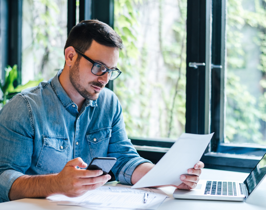 A man with glasses examining a document on his laptop.