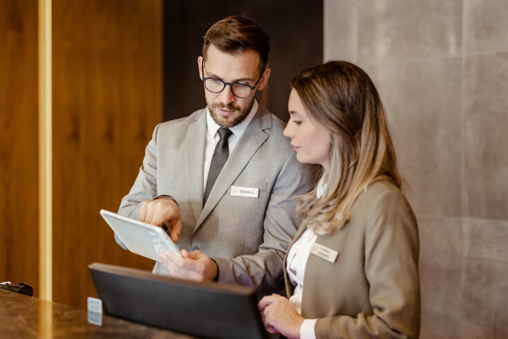 A man and woman dressed in business attire are positioned in front of a computer, focused on their work.